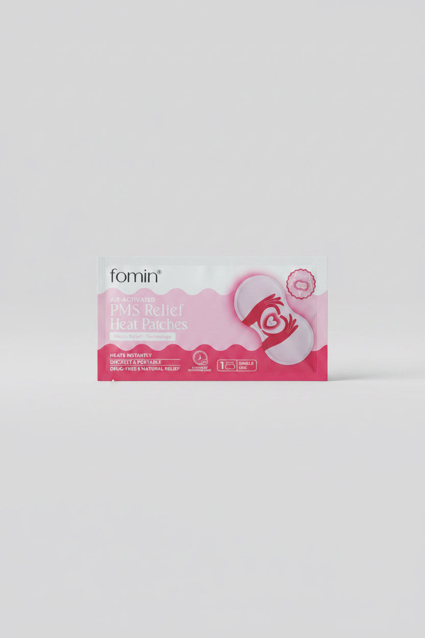A package of fomin Pain Relieving Heat Packs placed on a dark blue circular table. The packaging is light blue and pink with a graphic of a hand holding a heart-shaped heat pack.