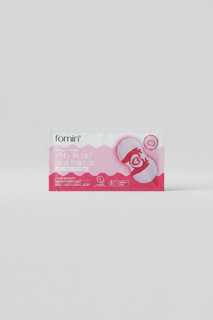 A package of fomin Pain Relieving Heat Packs placed on a dark blue circular table. The packaging is light blue and pink with a graphic of a hand holding a heart-shaped heat pack.