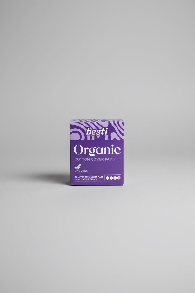 A box of Besti Organic Cotton Cover Pads sits on a dark blue patio table in front of a white wicker outdoor chair.
