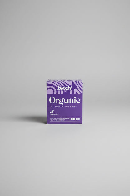 A box of Besti Organic Cotton Cover Pads sits on a dark blue patio table in front of a white wicker outdoor chair.